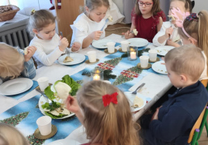 Dzieci siedzą za wspólnym stołem i jedzą potrawy Wigilijne