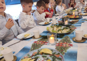 Dzieci siedzą za wspólnym stołem i jedzą potrawy Wigilijne