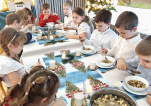 Dzieci siedzą za wspólnym stołem i jedzą potrawy Wigilijne