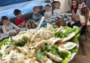Dzieci siedzą za wspólnym stołem i jedzą potrawy Wigilijne