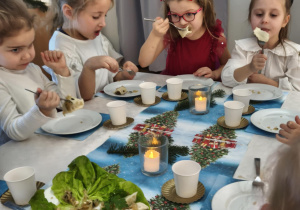 Dzieci siedzą za wspólnym stołem i jedzą potrawy Wigilijne