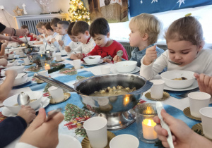 Dzieci siedzą za wspólnym stołem i jedzą potrawy Wigilijne