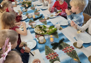 Dzieci siedzą za wspólnym stołem i jedzą potrawy Wigilijne