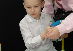 Na zdjęciu widzimy grupkę dzieci, które siedzą wraz z rodzicami przy stole ze słodkim poczęstunkiem.