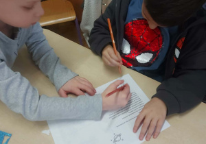 Zdjęcie przedstawia chłopców kolorujących kartkę