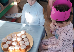 Dzieci siedzą przy stoliku, na którym stoją babeczki.