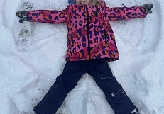 Zdjęcie przedstawia dziewczynkę robiącą aniołka na śniegu.