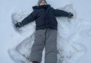 Zdjęcie przedstawia chłopca robiącego aniołka na śniegu..