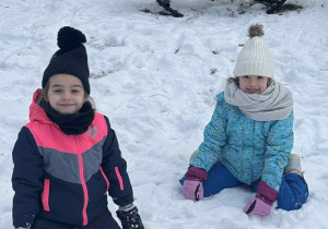 Zdjęcie przedstawia dwie dziewczynki siedzące na śniegu..