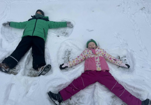 Zdjęcie przedstawia dwoje dzieci, robiących aniołki na śniegu.