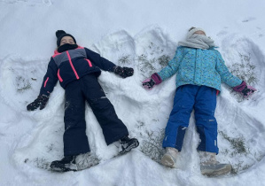 Zdjęcie przedstawia dwoje dzieci, robiących aniołki na śniegu.