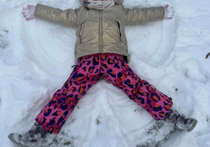 Zdjęcie przedstawia dziewczynkę robiącą aniołka na śniegu.