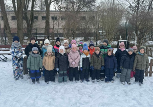 Zdjęcie przedstawia dzieci stojące na śniegu w zimowej scenerii.