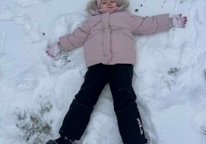 Zdjęcie przedstawia dziewczynkę robiącą aniołka na śniegu.