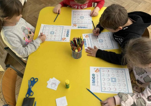 Zdjęcie przedstawia dzieci siedzące przy stoliku, podczas gry w bingo.