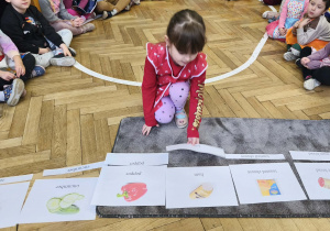 Na zdjęciu widzimy dziewczynkę, która przyporządkowuje nazwę w języku angielskim do ilustracji przedstawiającej dane produkty spożywcze.