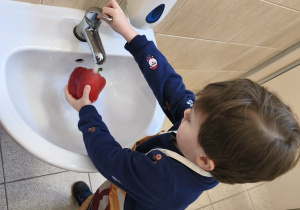 Na zdjęciu widzimy chłopca, który myje paprykę.