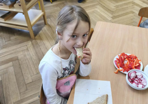 Na zdjęciu widzimy dziewczynkę, która zjada tosta.