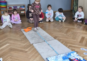 Na zdjęciu widzimy dziewczynkę, która idzie po smyczy. W ręku trzyma łyżkę ze smaczkiem.