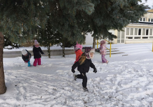 Na zdjęciu widzimy dzieci, które bawią się na śniegu w ogrodzie przedszkolnym.