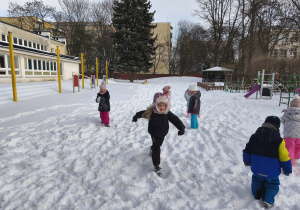 Na zdjęciu widzimy grupkę dzieci, które bawią się na śniegu.