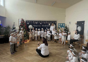 Zdjęcie przedstawia dzieci podczas gry na instrumentach. Dyryguje grą kobieta siedząca przed nimi.