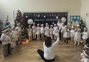 Zdjęcie przedstawia dzieci podczas gry na instrumentach. Dyryguje grą kobieta siedząca przed nimi.