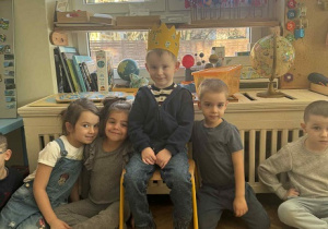 Zdjęcie przedstawia chłopca w koronie, siedzącego na krześle, wśród dzieci.