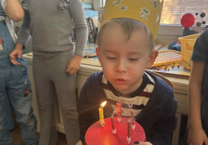 Zdjęcie przedstawia chłopca dmuchającego świeczki na torcie.