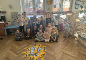 Zdjęcie przedstawia grupę dzieci siedzącą wokół Jubilata, przy słoneczku urodzinowym.