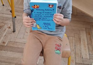 chłopiec w niebieskiej koronie siedzi na krześle, w rękach trzyma prezent