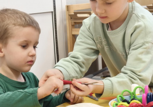 Chłopiec uczy młodszego kolegę wycinać nozyczkami