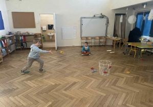 Zdjęcie przedstawia chłopca rzucającego woreczkiem do kosza.