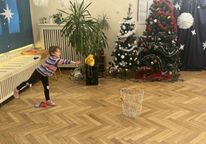 Zdjęcie przedstawia dziewczynkę rzucającą woreczkiem do kosza.