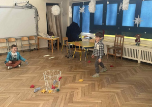 Zdjęcie przedstawia chłopca rzucającego woreczkiem do kosza.