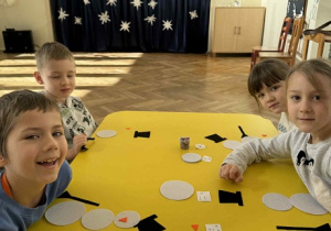 Zdjęcie przedstawia dzieci siedzące przy stoliku, podczas gry z kostką- układają bałwana z filcowych elementów.