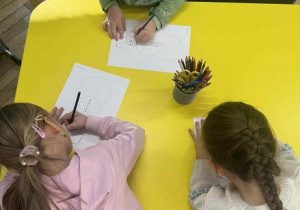 Zdjęcie przedstawia dzieci siedzące przy stole. Dzieci wykonują kartę pracy- łączą kropki tworząc postać bałwanka.