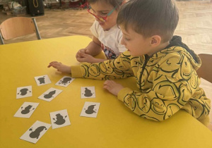 Zdjęcie przedstawia dzieci siedzące przy stole i oglądające obrazki- cienie bałwanków.