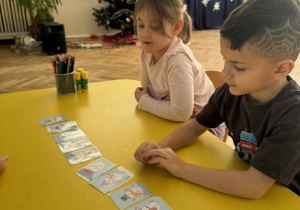 Zdjęcie przedstawia dzieci siedzące przy stole, na którym rozłożone są obrazki bałwanków.