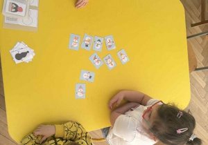 Zdjęcie przedstawia dzieci siedzące przy stole, na którym rozłożone są obrazki bałwanków.