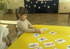 Zdjęcie przedstawia dziewczynkę dobierającą obrazki w pary.