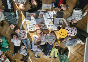 Na zdjęciu widzimy grupę dzieci które leżą jak "naleśniki". Pomiędzy nimi znajdują się ilustracje z prezentacji na temat naleśników - ich powstania, rodzaji itp.