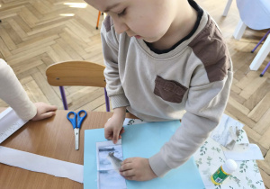 Na zdjęciu widzimy chłopca, który przykleja wycięte puzzle z niedźwiedziem polarnym.