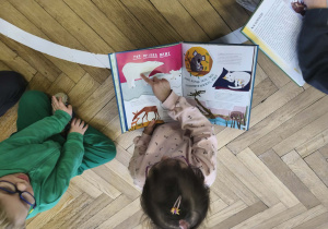 Na zdjęciu widzimy dziewczynkę, która poszukują w książce wiadomości i ilustracji o niedźwiedziu polarnym.