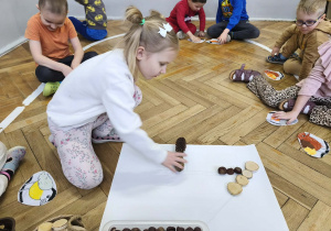 Na zdjęciu widzimy dziewczynkę, która układa szyszkę tworząc karmnik dla ptaków z materiału przyrodniczego.