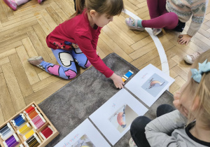 Na zdjęciu widzimy dziewczynkę, która przyporządkowuje tabliczki kolorystyczne do ilustracji przedstawiającej kowalika.