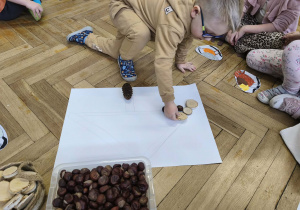 Na zdjęciu widzimy dziewczynkę, która układa drewienko tworząc karmnik dla ptaków z materiału przyrodniczego.