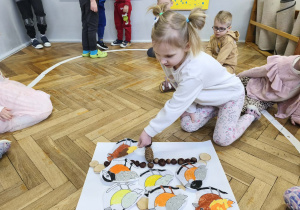 Na zdjęciu widzimy dziewczynkę, która kładzie wykonanego ptaszka na karmniku z materiału przyrodniczego.