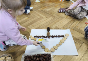 Na zdjęciu widzimy dziewczynkę, która kładzie wykonanego ptaszka na karmniku z materiału przyrodniczego.