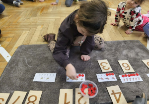 Na zdjęciu widzimy dziewczynkę, która kładzie odpowiednią ilość czerwonych żetonów.
